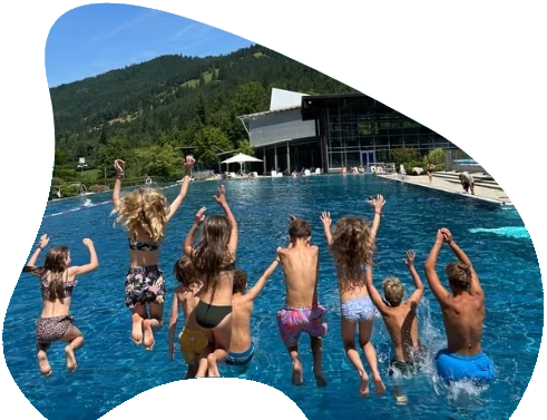 Kinder springen ins Schwimmbecken vor Bergkulisse